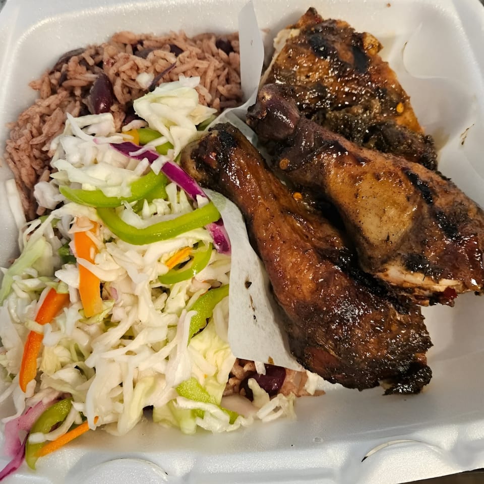 Topnotch Island Flavor Kitchen's Jamaican jerk chicken, rice and peas, and coleslaw in a takeout container.