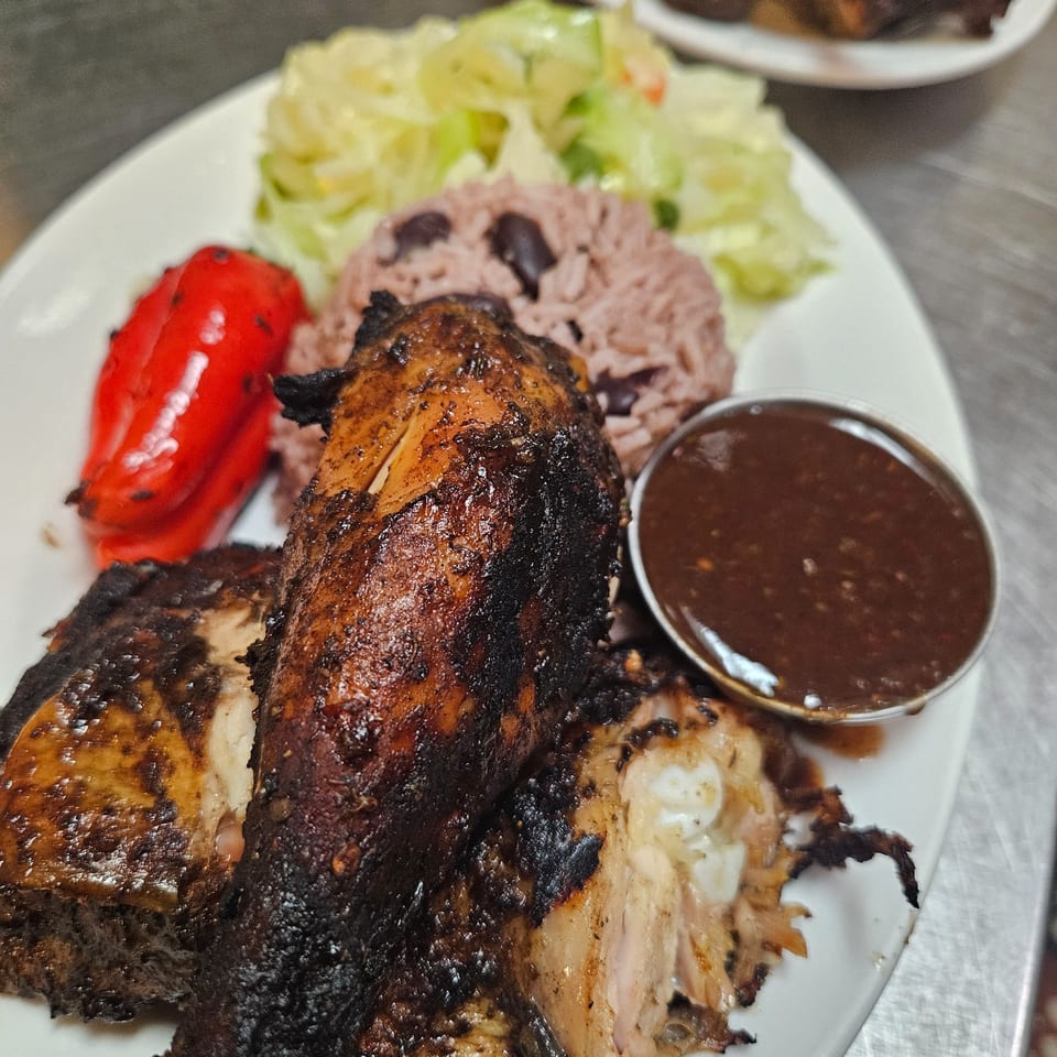A plate of Jamaican jerk chicken, rice and peas, steamed cabbage, and a red bell pepper.