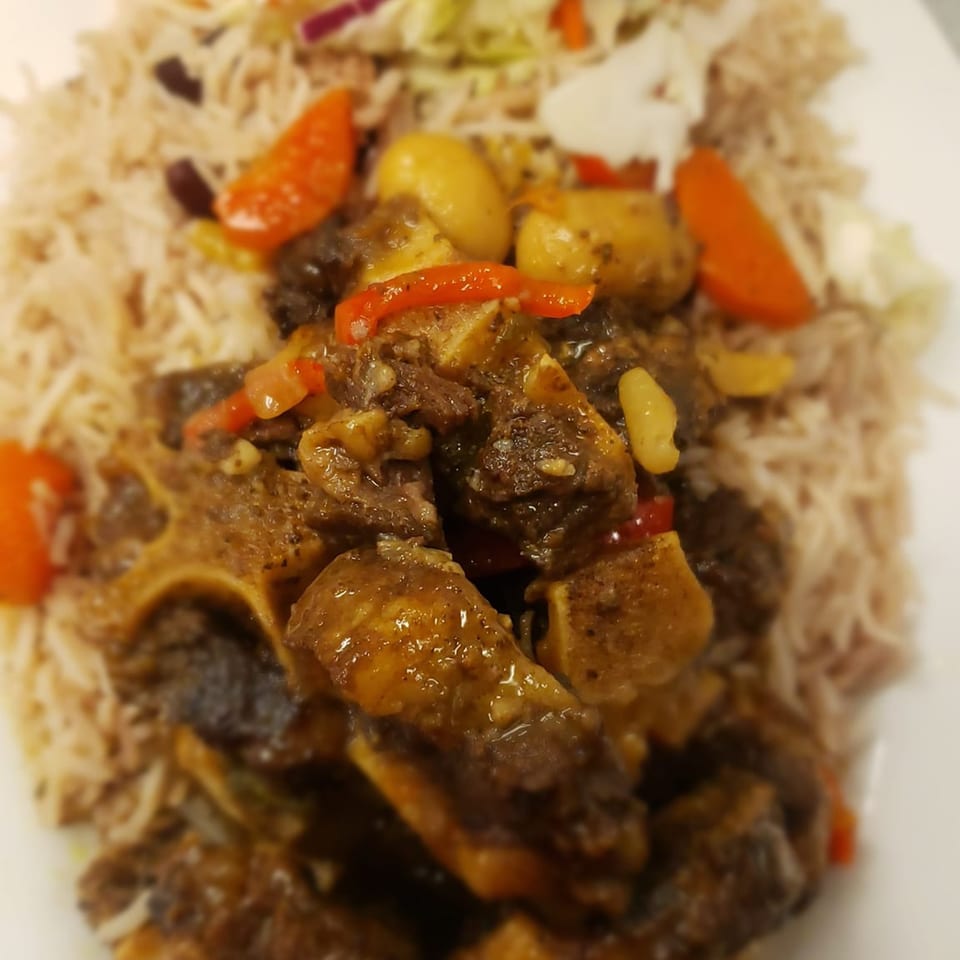 Close-up of Jamaican oxtail stew with rice and peas, garnished with red peppers and potatoes.