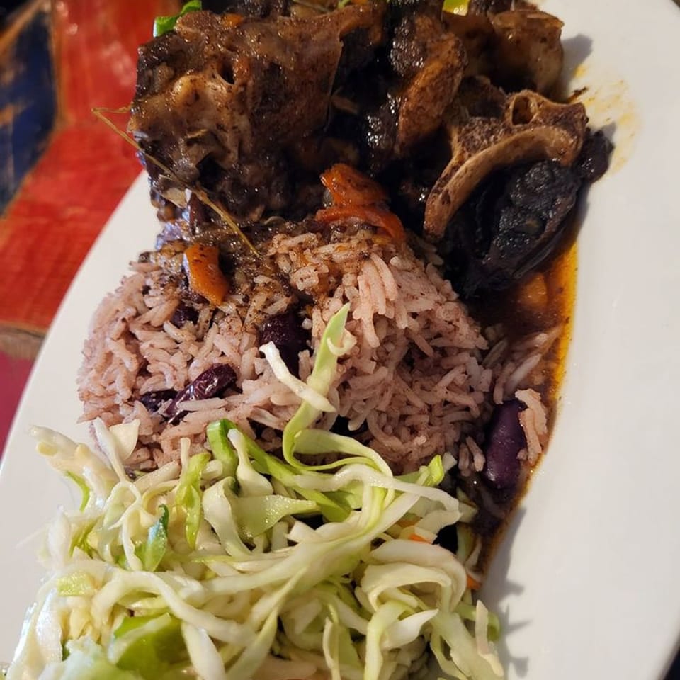 Jamaican oxtail with rice and peas, and a side of shredded cabbage on a white plate.