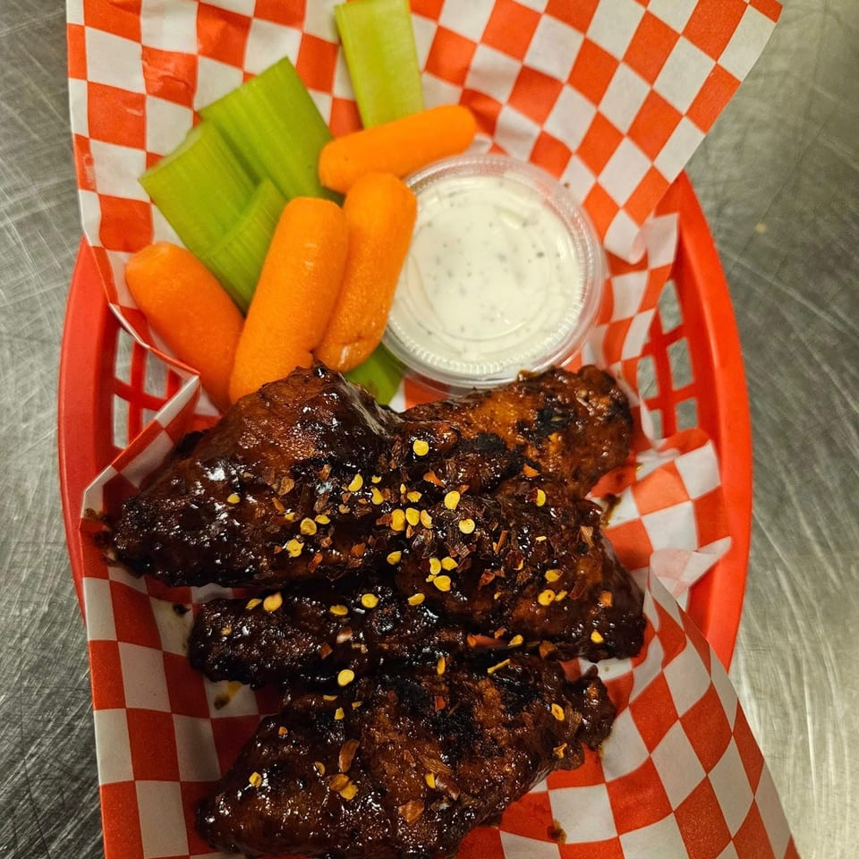 Topnotch Island Flavor Kitchen's Jamaican jerk wings with celery, carrots, and ranch in a red basket.