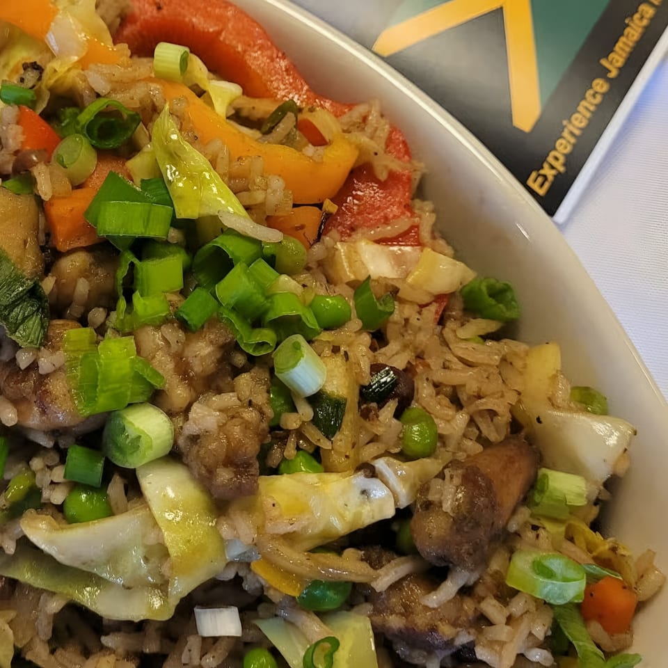 Close-up of Jamaican fried rice with vegetables, chicken, and scallions in a white bowl.