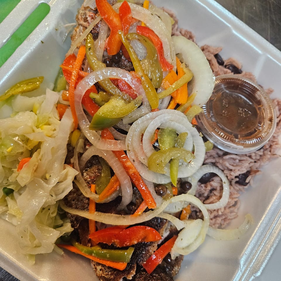 Jamaican brown stew fish topped with colorful bell peppers and onions, served with rice and cabbage.