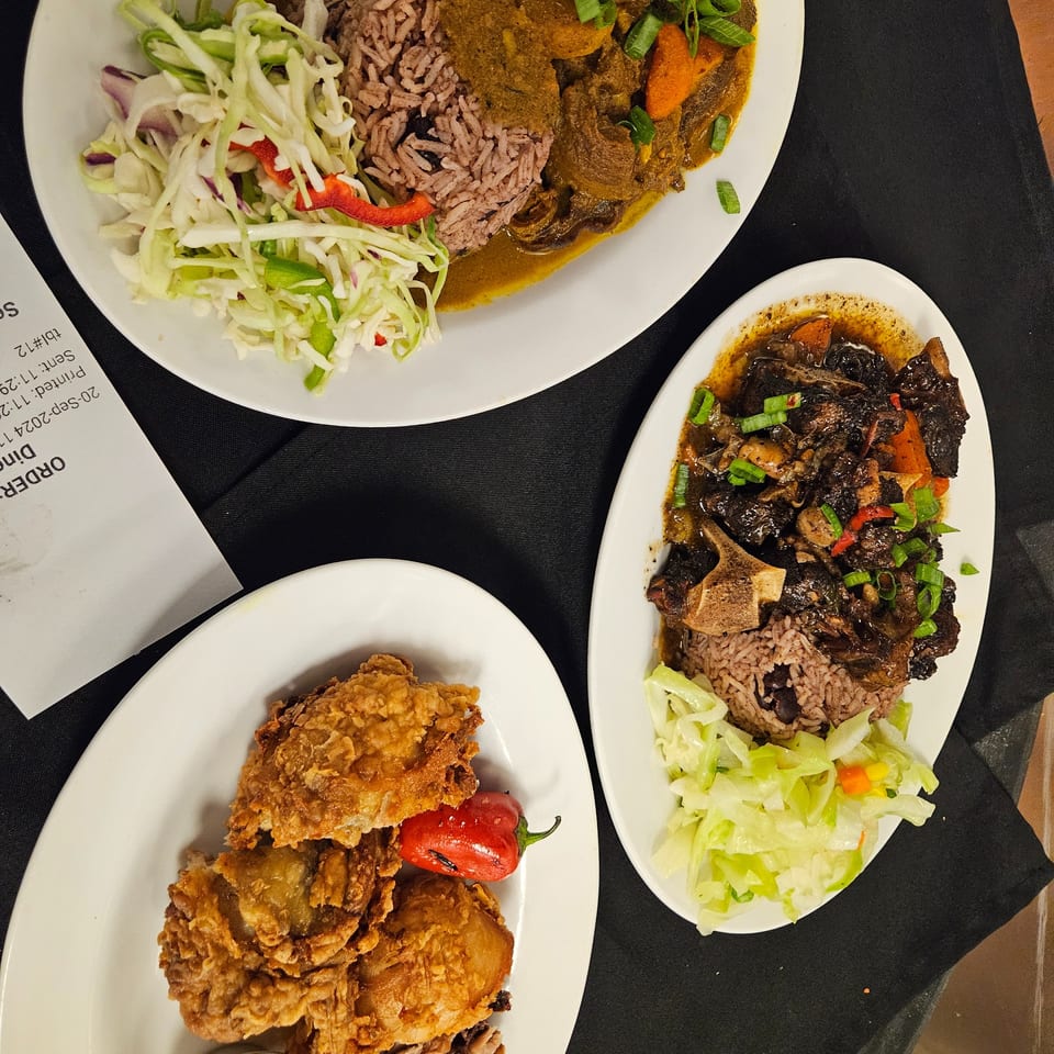 Three plates of Jamaican food, including curry, oxtail, and fried chicken, with rice and cabbage.